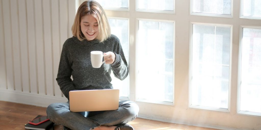 Девојка која работи од дома на лаптоп и пие кафе
